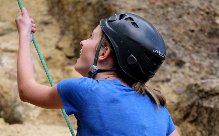 A person wearing a helmet holds onto a rope as they belay a climber.